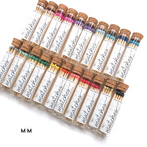 May include: An assortment of glass tubes filled with long wooden matches. Each tube has a cork stopper and a label that reads "matches." The match heads are various colors, including pink, purple, blue, green, yellow, orange, red, and black.