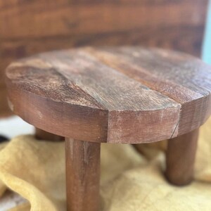 Puede incluir: Un peque&ntilde;o soporte redondo de madera para plantas con tres patas cil&iacute;ndricas. El soporte est&aacute; hecho de madera marr&oacute;n oscuro con vetas visibles y un acabado natural. El soporte est&aacute; dise&ntilde;ado para elevar plantas u otros objetos decorativos.