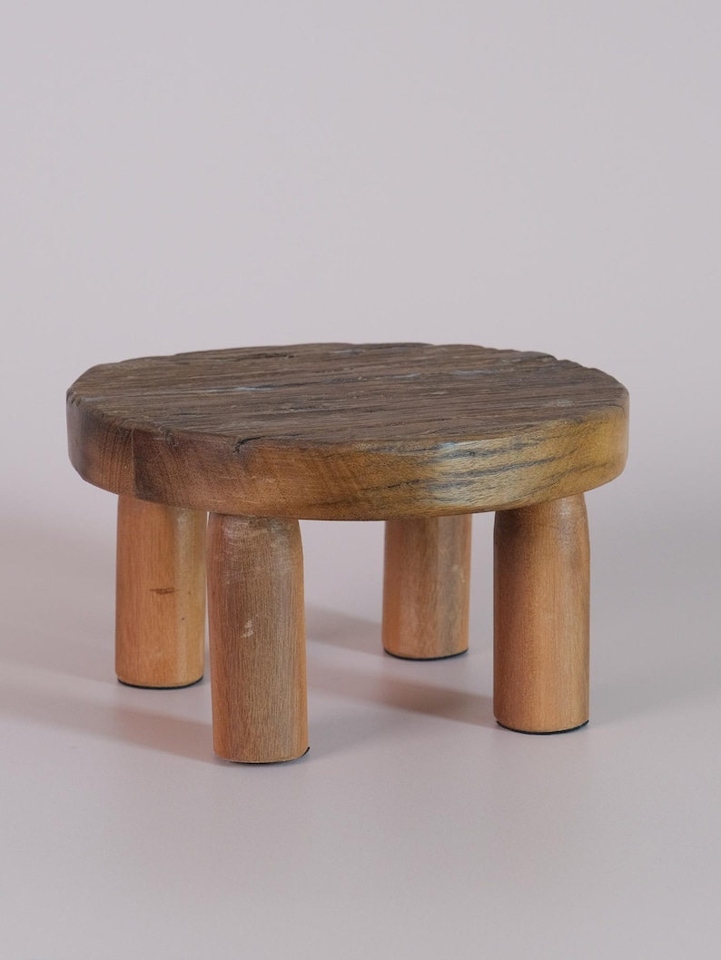 Puede incluir: Un peque&ntilde;o taburete redondo de madera con una parte superior texturizada y desgastada y cuatro patas cil&iacute;ndricas. El taburete est&aacute; hecho de madera clara con un acabado natural y tiene aproximadamente 25 cm de di&aacute;metro.