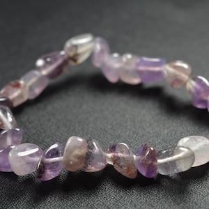 May include: A purple and clear crystal bracelet made of small, flat, irregular shaped stones.