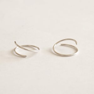 May include: A pair of silver double hoop earrings. The hoops are thin and delicate, and they are twisted together to create a unique and modern look.
