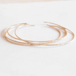 Puede incluir: Tres pulseras de metal martillado de color dorado apiladas una encima de la otra.