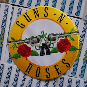 May include: A yellow and white embroidered patch featuring the words "Guns N' Roses" and a pair of crossed revolvers wrapped in barbed wire and roses.