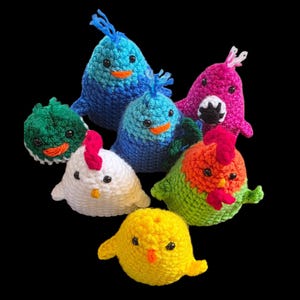 May include: A collection of handmade crochet birds and chicks in various colors, including blue, green, white, yellow, orange, and pink. Each bird has a unique design with small black eyes and orange or red beaks and crests. The toys are arranged against a black background.