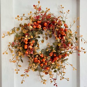 May include: A fall-themed wreath with orange and red berries and green and yellow leaves.