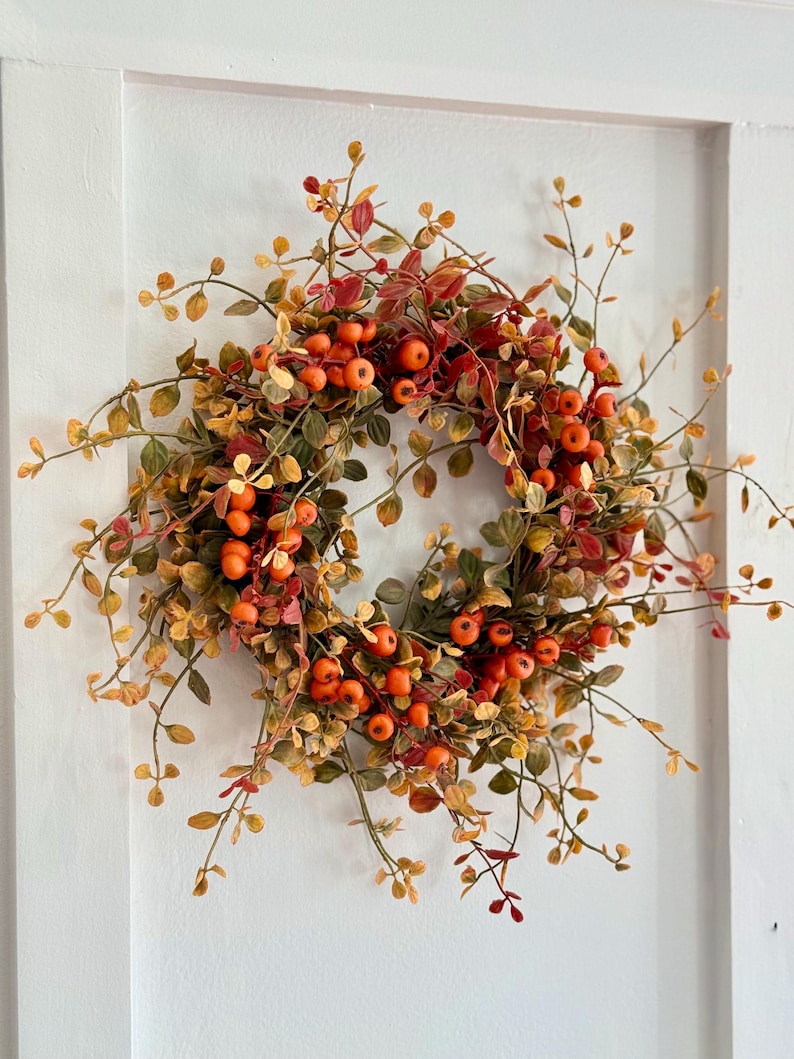 May include: A fall-themed wreath with orange and red berries and green and yellow leaves.