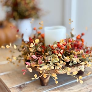 May include: A wooden pedestal with a fall-themed wreath featuring faux leaves and berries. The wreath is decorated with small, orange-red berries and leaves in shades of green, yellow, and orange.