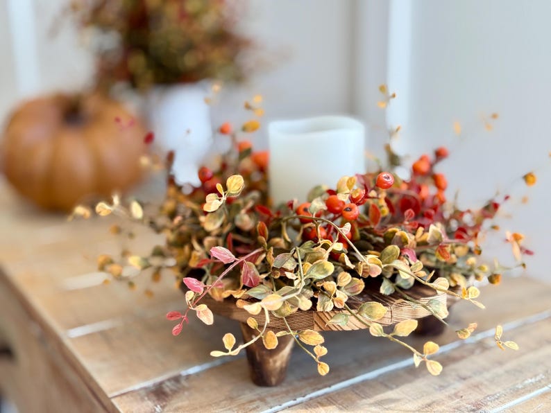 May include: A wooden pedestal with a fall-themed wreath featuring faux leaves and berries. The wreath is decorated with small, orange-red berries and leaves in shades of green, yellow, and orange.
