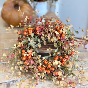 May include: A fall-themed wreath with orange berries and green and red leaves. The wreath is made of faux foliage and is perfect for decorating your home for the autumn season.