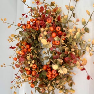 May include: A fall-themed wreath with orange berries and green and brown leaves.