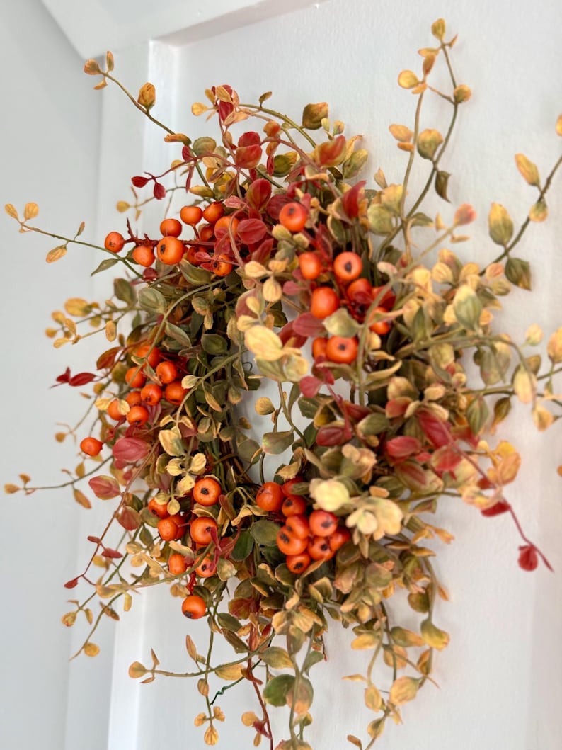 May include: A fall-themed wreath with orange berries and green and brown leaves.