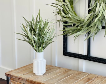 Tall grassy tabletop centerpiece floral arrangement, airy long grass stems with white spear flowers, matt white ceramic vase