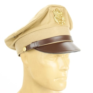 Peut inclure: Casquette de style militaire beige avec visière et bandeau en cuir marron. Le chapeau présente un emblème doré et un bouton doré sur le côté. Accessoire militaire classique.