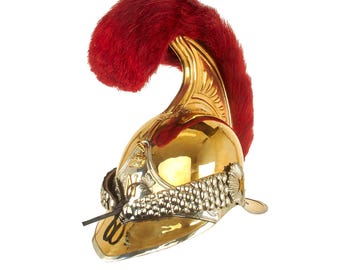 May include: A polished gold-colored helmet with a red plume. The helmet features ornate silver-colored detailing around the base and a curved design. The helmet is likely a historical or ceremonial piece.