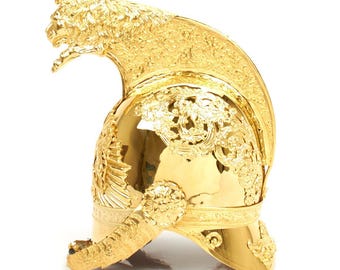 May include: A gold-colored helmet with intricate detailing. The helmet features a lion's head crest and ornate floral and foliate patterns. The design is highly reflective, suggesting a polished metal finish. The helmet's style evokes historical military headwear.