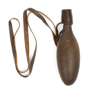 May include: A brown leather flask with a matching leather strap. The flask has a rounded, elongated shape and a small, cylindrical neck. The strap is attached to the neck and extends to form a loop for carrying. The leather appears worn.