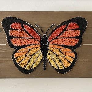 Pode incluir: Uma borboleta de arte de fio com cores laranja, amarelo e preto em um fundo de madeira.