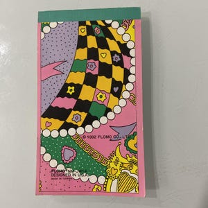 May include: A vintage notepad with a pink border and a colorful design. The cover features a checkerboard pattern in yellow and black, along with hearts, flowers, and other decorative elements. Text includes "1992 FLOMO CO., LTD." and "DESIGNED IN U.S.A."