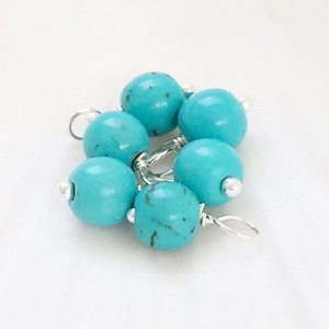 May include: A cluster of six turquoise blue beads with silver wire accents. The beads are round and have a smooth, polished finish.