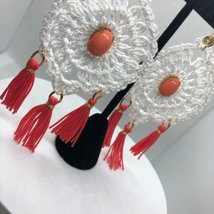 May include: White crocheted earrings with coral-colored beads and red tassels.