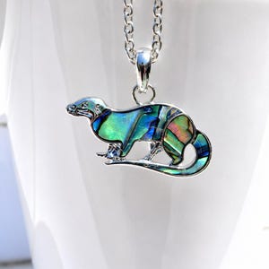 Otter necklace with colourful abalone shell pendant displayed on a white ceramic mug, shown on a silver-tone trace chain.