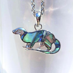 Otter necklace with colourful abalone shell pendant displayed on a white ceramic mug, shown on a silver-tone trace chain.