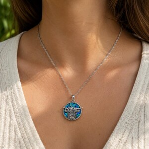 Highland cow abalone shell necklace worn on a trace chain, featuring a silver-tone cow pendant with blue and green paua shell detail.