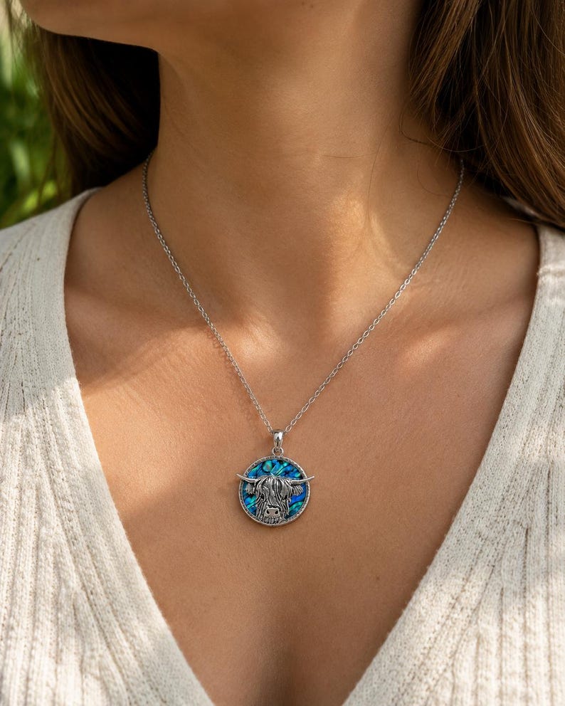 Highland cow abalone shell necklace worn on a trace chain, featuring a silver-tone cow pendant with blue and green paua shell detail.