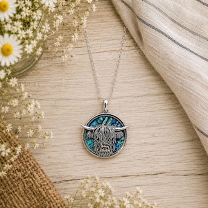 Abalone Highland Cow necklace with trace chain flat lay on a rustic wooden surface with wildflowers and soft neutral linen styling.
