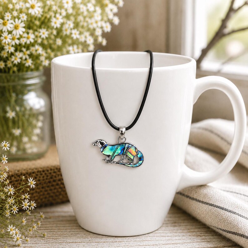 Paua shell otter pendant necklace displayed on a white ceramic mug with a black cord necklace option.