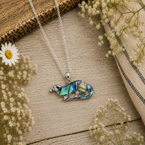 Paua shell otter necklace arranged on a rustic botanical flat lay with daisies and delicate white flowers on a wooden background.