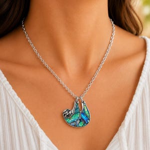 Abalone sloth necklace worn on a silver trace chain, showing an iridescent paua shell sloth pendant against a neutral blouse and soft natural background. ai model