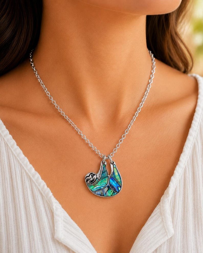 Abalone sloth necklace worn on a silver trace chain, showing an iridescent paua shell sloth pendant against a neutral blouse and soft natural background. ai model