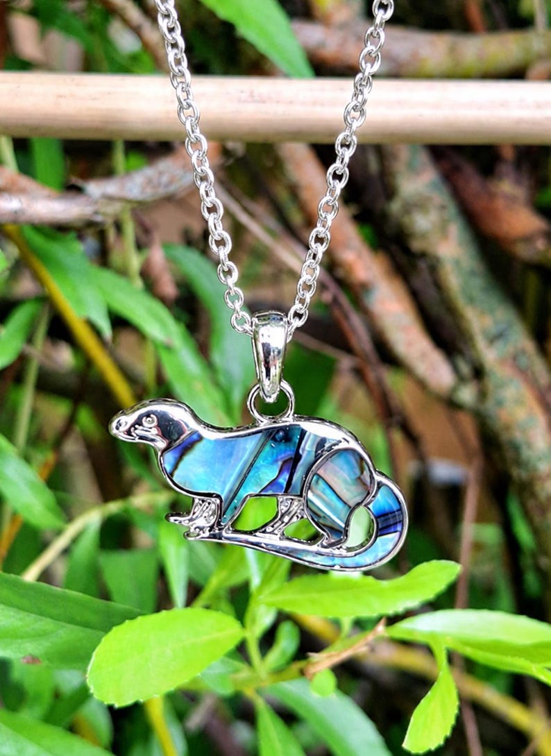 Abalone shell otter necklace hanging outdoors amongst natural greenery, featuring an iridescent paua shell otter pendant on a trace chain.