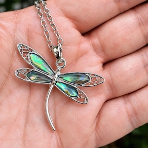 Close-up of an abalone shell dragonfly necklace resting on a hand showing size, colour and intricate silver detailing.
