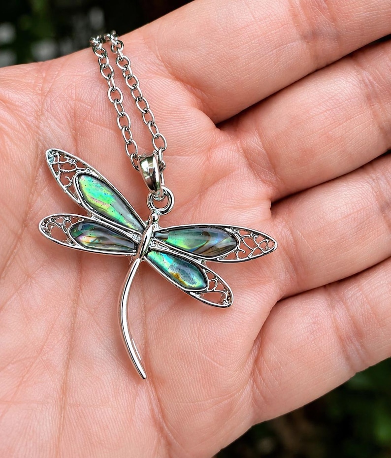 Close-up of an abalone shell dragonfly necklace resting on a hand showing size, colour and intricate silver detailing.