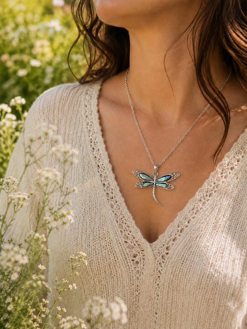 Woman wearing an abalone shell dragonfly necklace on a silver chain outdoors in soft natural sunlight.