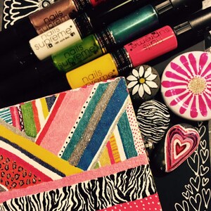 May include: A close-up of a colorful, patterned box with a variety of nail polishes in different colors, including pink, green, and black. The nail polishes are labeled "Nails Supreme".