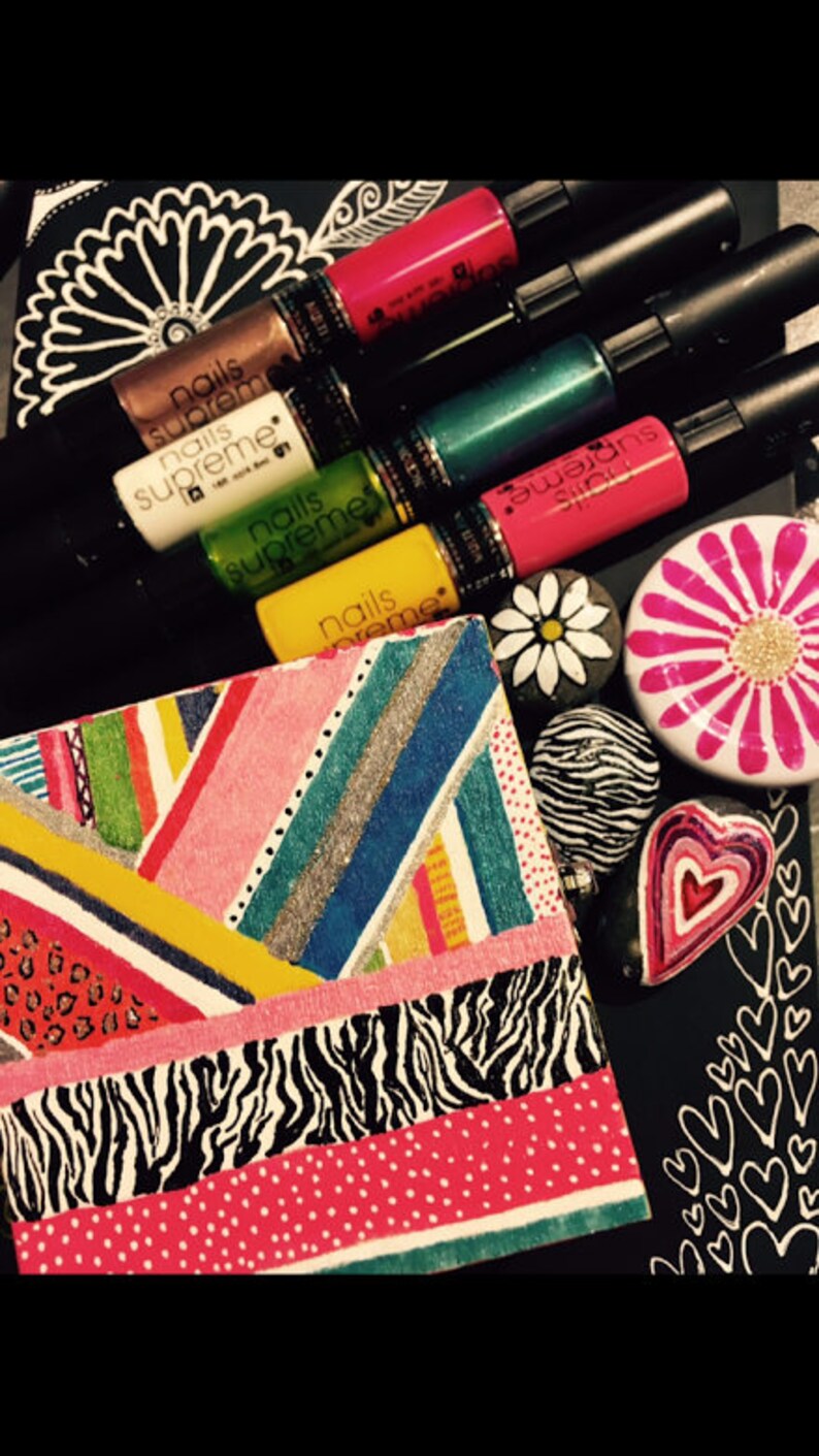 May include: A close-up of a colorful, patterned box with a variety of nail polishes in different colors, including pink, green, and black. The nail polishes are labeled "Nails Supreme".