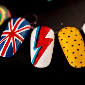 May include: Six painted fingernails with different designs. The designs include a swirl, a Union Jack, a lightning bolt, polka dots, a geometric pattern, and a striped pattern.