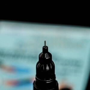 May include: Close-up of the tip of a black marker pen with a fine point.
