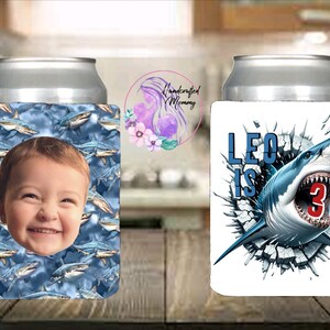 May include: Two can coolers. One features a smiling child's face surrounded by a shark pattern. The other has a shark bursting through a wall with the text "Leo is 3".