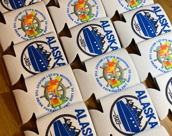 May include: White drink koozies with the word "ALASKA" in blue, a blue ship graphic, and the text "2023". The koozies also feature a ship's wheel and the phrase "I BOUGHT THE DRINK PACKAGE".