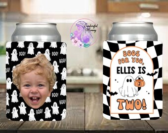 May include: Two cylindrical can coolers. The left cooler features a black background with white ghost illustrations, the word BOO, and a photograph of a young child. The right cooler has a black and white checkered pattern, a ghost holding a pumpkin with the number 2, and the text BOOS FOR YOU, ELLIS IS TWO!