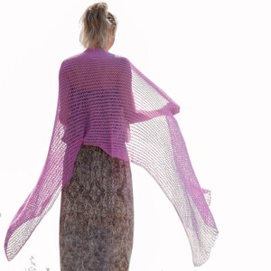May include: A woman wearing a long, flowing, pink crochet shawl. The shawl is draped over her shoulders and is flowing in the wind.