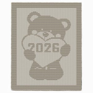 Könnte beinhalten: Eine beige gestrickte Decke mit einem Bärenmuster, das ein Herz hält. Das Herz enthält die Zahlen "2026". Die Decke hat einen gestreiften Rand und das Bärenmuster besteht aus horizontalen Linien.