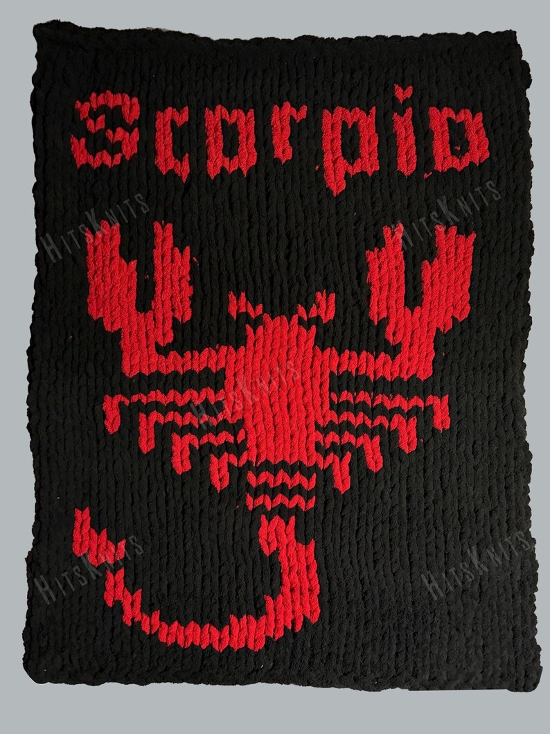 May include: A rectangular black knit blanket featuring a large red scorpion graphic centered in the middle. The word "Scorpio" is stitched in red letters above the scorpion. The texture of the yarn is thick and chunky throughout the piece.