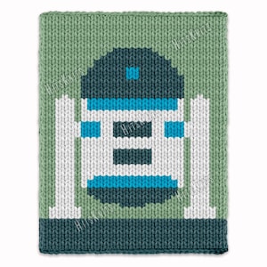 Könnte beinhalten: Eine gestrickte Decke mit einem pixeligen Roboterdesign in Blau, Weiß und Grün. Der Roboter befindet sich vor einem grünen Hintergrund mit weißen vertikalen Balken. Die Decke hat einen dunkelgrünen Rand. Das Design erinnert an eine bekannte Science-Fiction-Figur.