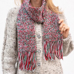 May include: A red, white, and green knitted scarf with fringe. The scarf is made of a soft, chunky yarn and has a speckled pattern.