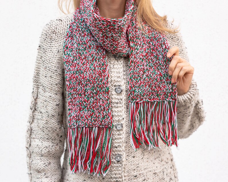 May include: A red, white, and green knitted scarf with fringe. The scarf is made of a soft, chunky yarn and has a speckled pattern.